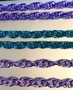 The photo shows a closeup of lengths of colorful chainmail chain displayed on a table.