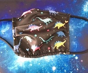 A cloth face mask made from black fabric that is printed with colorful drawings of various dinosaurs.