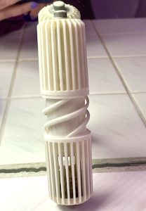 A springy white plastic toilet paper holder rod rests on a tiled counter.