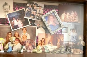 A shadowbox displays more than a dozen photos of family and friends, a mix of vintage and contemporary snapshots. Underneath are posed a row of little collectible figures, including wild cats and some zombies.