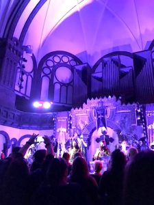 The German medieval rock band Corvus Corax, washed in purple lighting, perform inside a castle-like church.