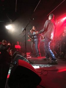 Members of the folk-punk band The Men They Couldn't Hang playing on a stage lighted in red.