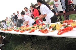 At an outdoor buffet, a crowd of wine drinkers lines up alongside a row of long tables, on which are displayed freshly cooked lobsters and vegetables.