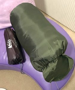 A closeup of an army green sleeping bag inside its nylon stuff sack.