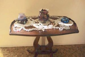 A silver Christmas garland made of woven beads is displayed on a small decorative wooden table.