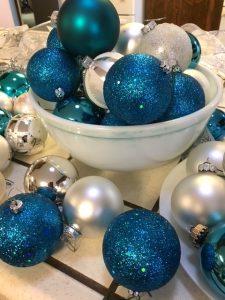 A selection of round blue, silver and white glass Christmas ornaments are piled on a kitchen counter, some in a Pyrex bowl.