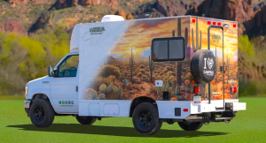 A CruiseAmerica ultra-compact RV is shown parked on grass, with a hilly landscape in the background.