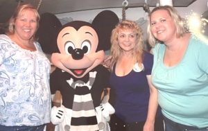 Three blond women pose with a costumed Mickey Mouse.