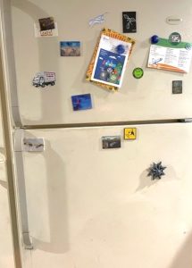 A traditional-looking beige kitchen refrigerator has a freezer door on top and a refrigerator door underneath. It is covered in decorative magnets, a couple of which hold important papers.