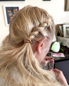 A blonde woman, photographed from behind/over her shoulder, is handling a pair of wire-framed glasses and accidentally smudging them.