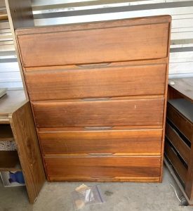 A tall brown dresser in a storage unit, with other furniture stowed next to it.