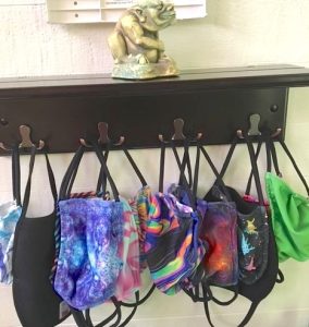A row of colorful cloth masks from Electrothreads hangs from the hooks of a small wall shelf. On top of the shelf sits a little sculpture of a gargoyle.