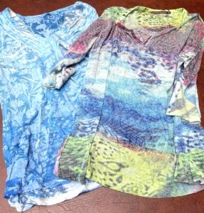Two bright, colorful shirts featuring very busy patterns are laid out on a table.