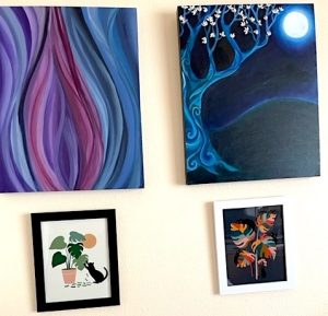 Four artworks are hung on a cream-colored wall. The top two are paintings; on the left is an abstract work of purples, blues, and dark pinks, while on the right is a stylized tree and full moon on a dark, moody background. The bottom artworks are two stylized prints featuring cats and monstera plants.