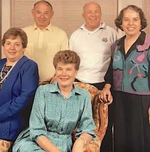 In this vintage family snapshot, two older men and three older women pose with warm smiles.