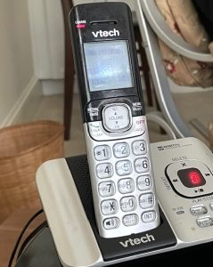 A silver-and-black cordless landline phone sits in its charging cradle.