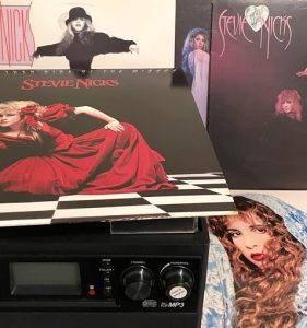 Five vinyl albums by Stevie Nicks are arranged around a vinyl-to-MP3 converter, which features a record player integrated on top of a recording module. The module has dial controls, buttons, and a digital display.
