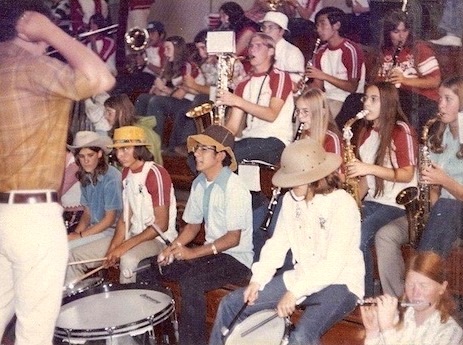 In this vintage snapshot, a couple of dozen teenagers, many wearing silly hats, play their band instruments during a high school pep rally.